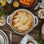 Golden-brown chicken pot pie with flaky crust surrounded by fresh green salad, creamy mashed potatoes, honey-glazed carrots, and a cozy rustic table setting.