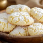 A plate of freshly baked Cool Whip Cookies with powdered sugar on top, placed on a rustic wooden table.