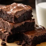 A stack of fudgy Lunch Lady Brownies topped with glossy chocolate frosting, sitting on a rustic wooden board.