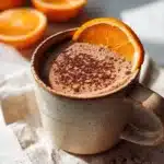 A cup of blood orange hot chocolate topped with whipped cream and orange zest.