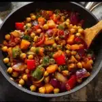 Colorful vegetable chickpea skillet dish garnished with fresh herbs.