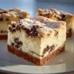 Delicious cannoli cheesecake bars topped with chocolate chips and cream.