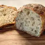 Freshly baked sourdough seeded sandwich bread on a wooden cutting board.