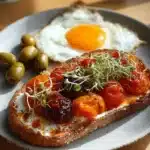 Plate of roasted tomato toast topped with a sunny side up egg, garnished for flavor.