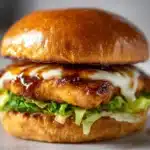Delicious grilled chicken burger with cheese on a bun, garnished with fresh lettuce.