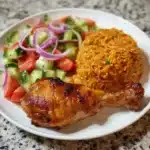 Plate of Jollof Rice with grilled chicken and a side of fresh salad.